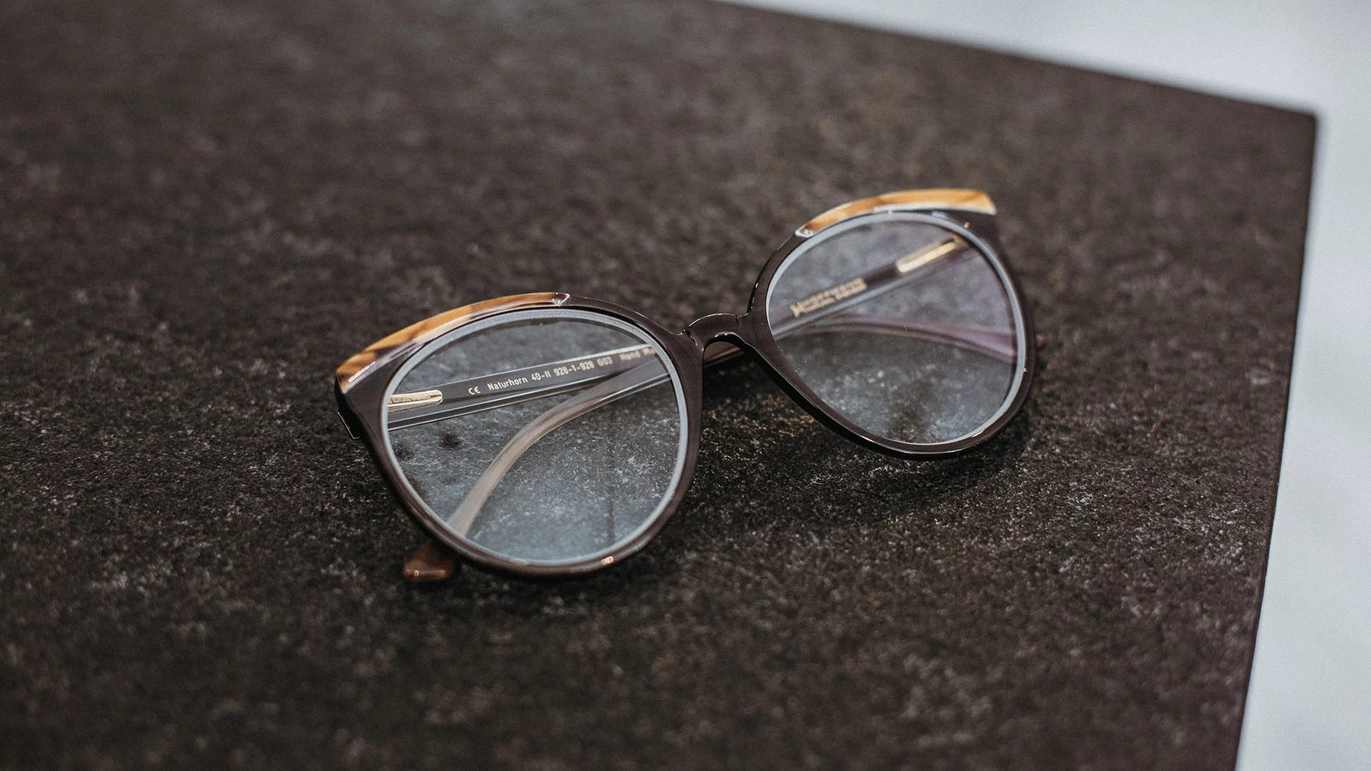 Braune Naturhornbrille mit hellen Akzenten von Hoffmann Natural Eyewear, die auf einem braunen Untergrund liegt.