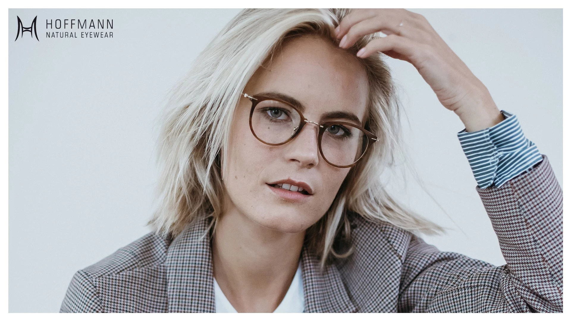 Nahaufnahme von einem Female Model mit schulterlangen Haaren, das einen Blazer und eine runde, braune Fassung von Hoffmann Natural Eyewear trägt.