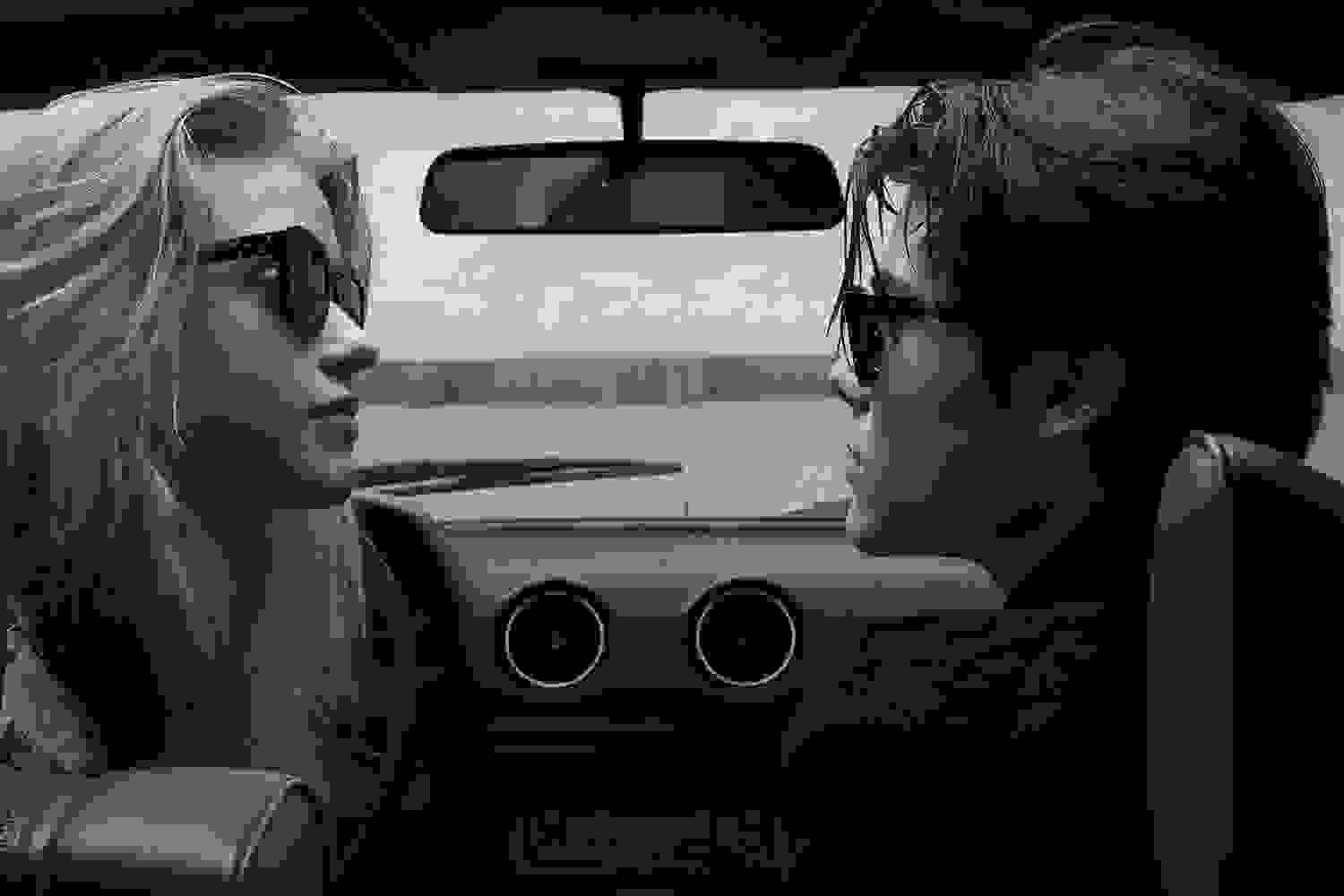 Schwarz-weiß Aufnahme von einem Male Model und einem Female Model, die sich im Auto gegenüber sitzen und eine Ahlem Sonnenbrille tragen.