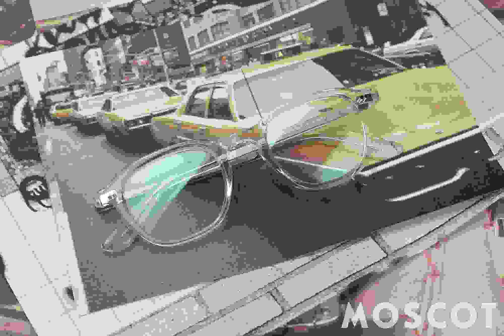 Moscot Korrekturbrille mit durchsichtigem Rahmen, die auf mehreren Fotoausdrücken liegt.