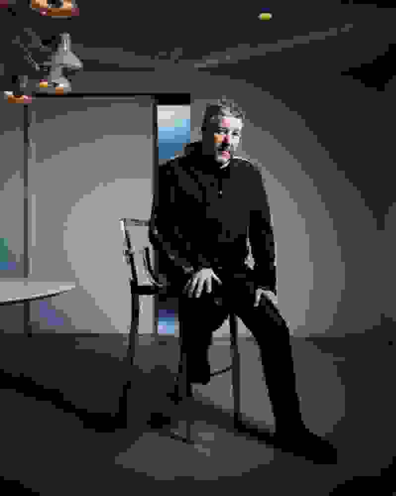 Philippe Starck, der in einem dunkeln Raum auf einem Stuhl sitzt und in die Kamera blickt.